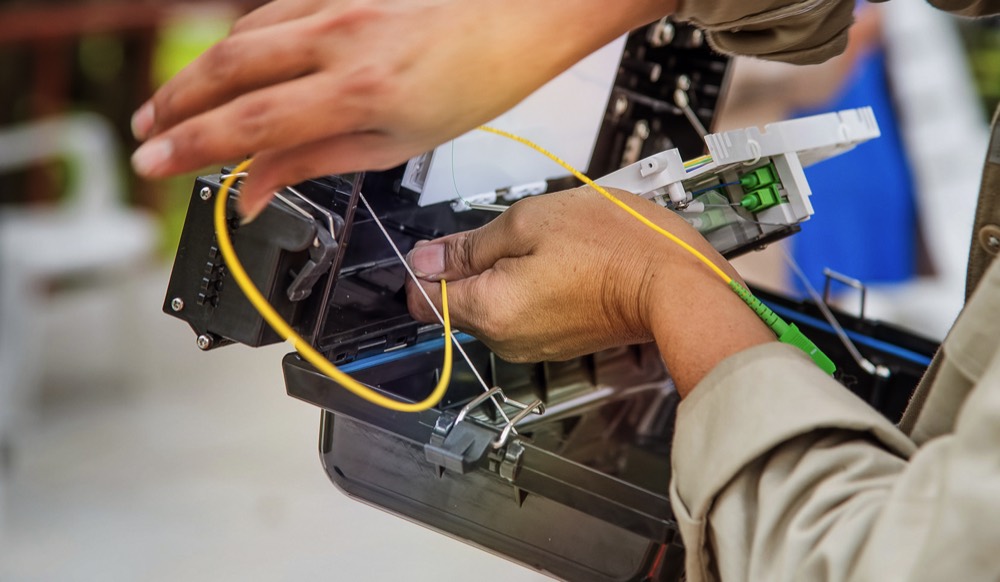 Technician splicing yellow fiber-optic cable in a distribution terminal